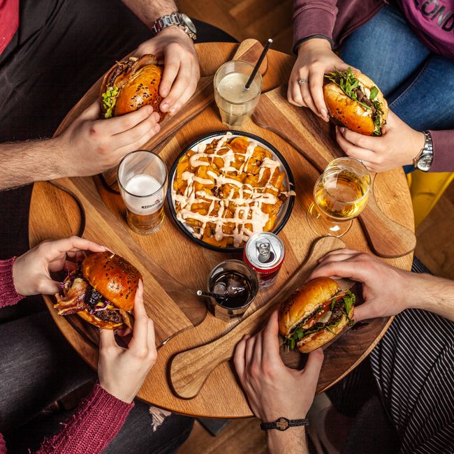 Friends gathered around a table sharing burgers and fries with drinks, creating a casual dining atmosphere.