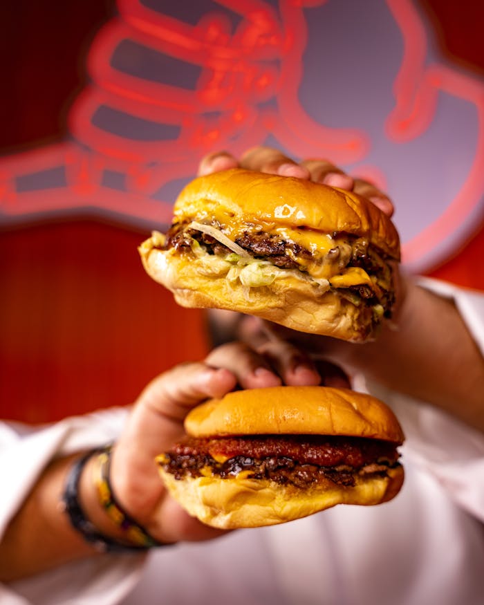 Close-up of two delicious burgers being held, showcasing juicy beef patties and melted cheese.